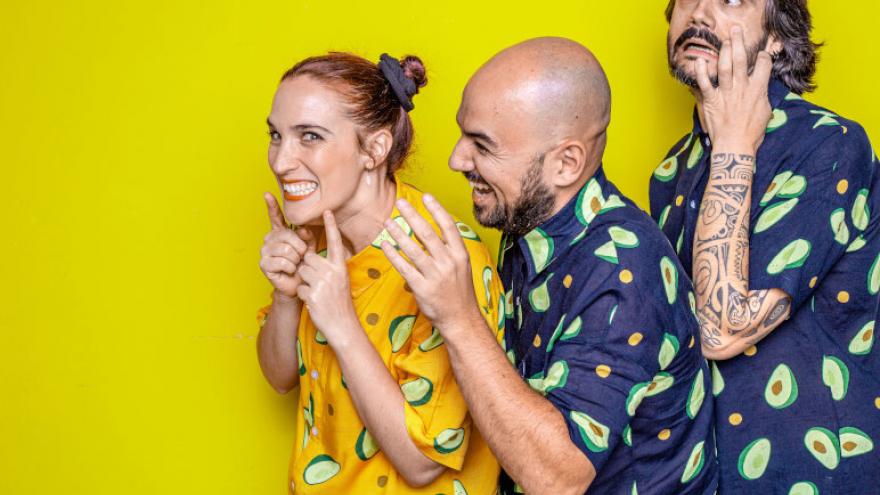 Fotografía de Arigato sobre un fondo amarillo, los tres visten camisas de guacates