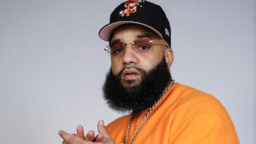 Foto Chris lleva una sudadera naranja con gorra y gafas de sol ahumadas, junta sus manos en un aplauso