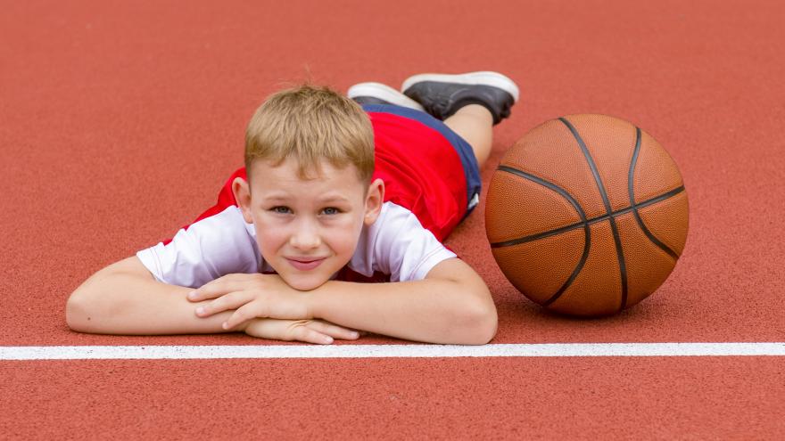 Niño tumbado sobre la pista junto a pelota de baloncesto