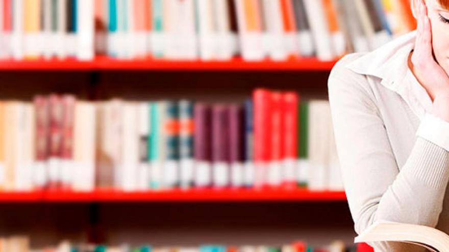 Chica joven estudiando, con balda de libros al fondo