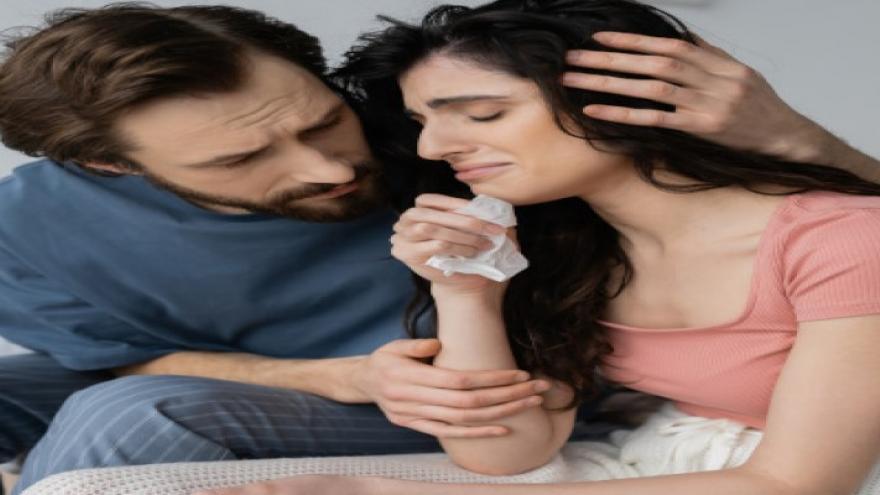 Mujer con expresión de dolor siendo abrazada por pareja