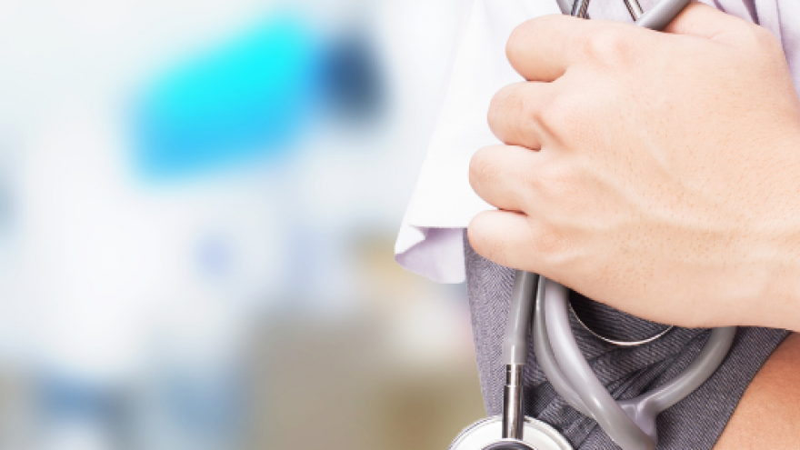 Primer plano a la derecha del torso de un profesional médico con bata blanca con los brazos cruzados y en la mano un fonendoscopio