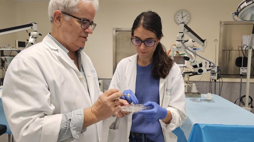 Dos profesionales con bata blanca observan un material que uno de llos hombre sostiene en una pinza