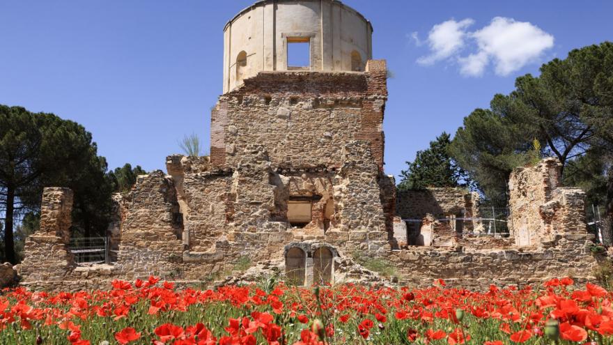 edificio con torreón semicircular y perímetro de piedra con un campo de amapolas en primer plano