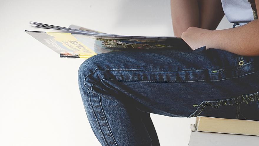 Joven sentada sobre libros y sujetando un libro en las manos