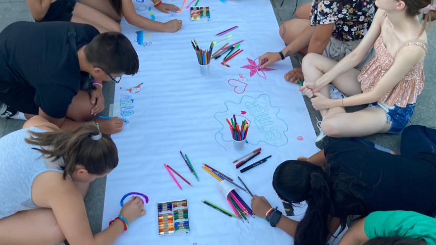 jóvenes pintando con colores en el suelo en un papel gigante