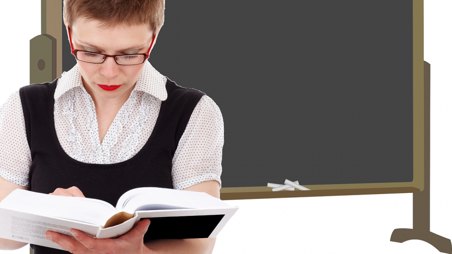 Profesora lee un libro con un fondo de pizarra de tiza