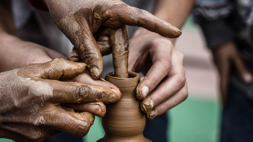 Dos personas trabajando una figura de cerámica en el torno