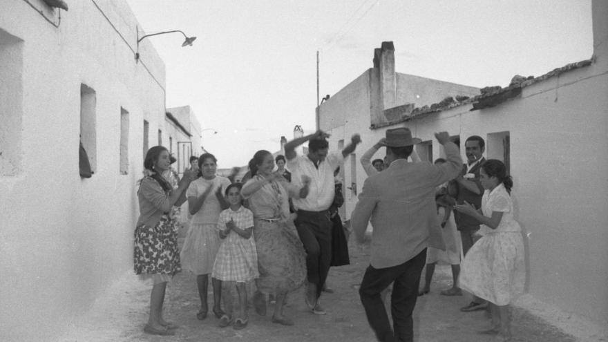 Un grupo de hombres, mujeres y niños bailando flamenco y dando palmas en un poblado