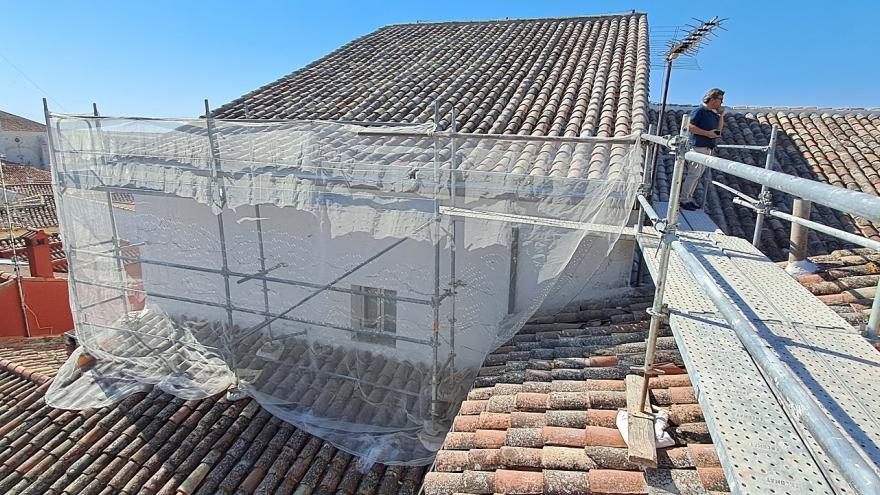 fachada cubierta por andamios, cubiertas de teja e iglesia al fondo