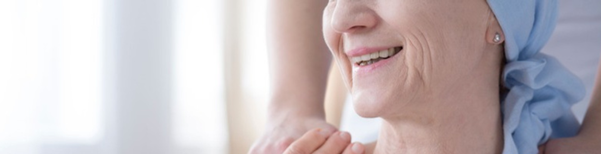 Paciente de cáncer. a la derecha detalle del rostro de una mujer con pañuelo en la cabeza y sus manos que agarran la mano de otra persona