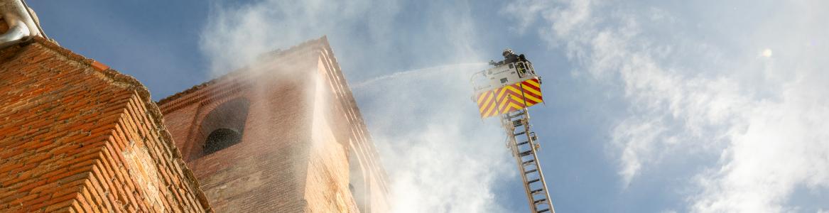 Un bombero en una escala extingue el humo que sale del torreón de una iglesia