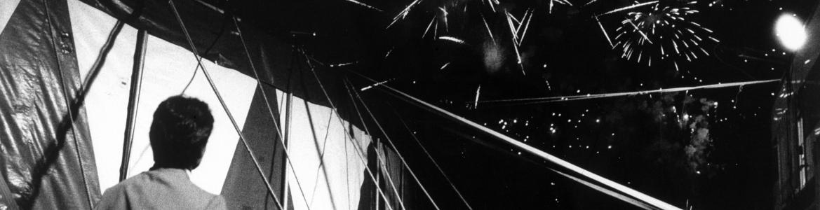 José Muñoz. Circo Mundial, Bilbao, 1992 Colección Museo CA2M ©VEGAP. Madrid, 2025 Hombre contemplando una carpa de circo bajo un cielo cubierto de fuegos artificales