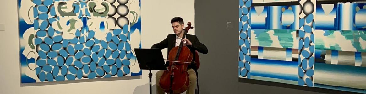 Violonchelista tocando frente a dos cuadros abstractos