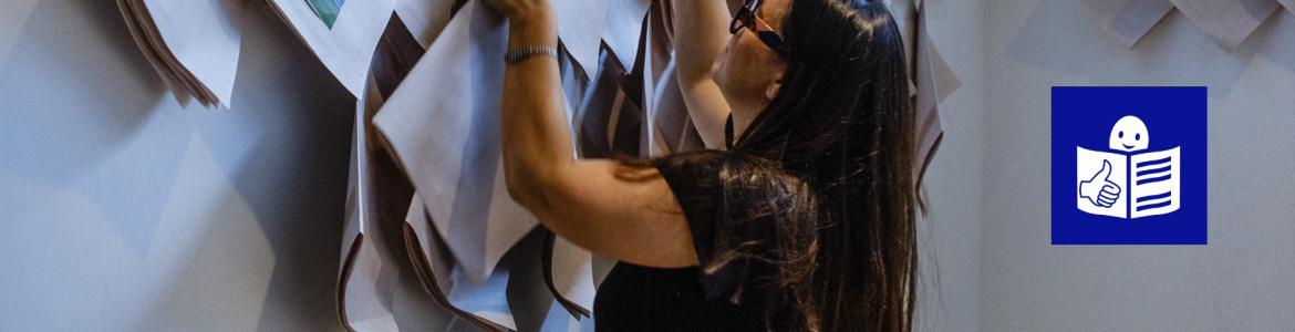 Lectura Fácil en exposiciones Mujer joven con gafas cogiendo un folleto en papel de la pared