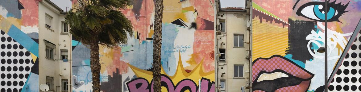Calle de una ciudad con edificios con grafitis, palmeras y coche rojo