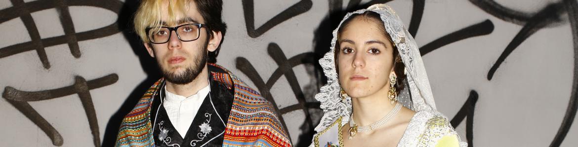 Dos jóvenes vestidos con traje regional de Valencia posando frente a un grafiti