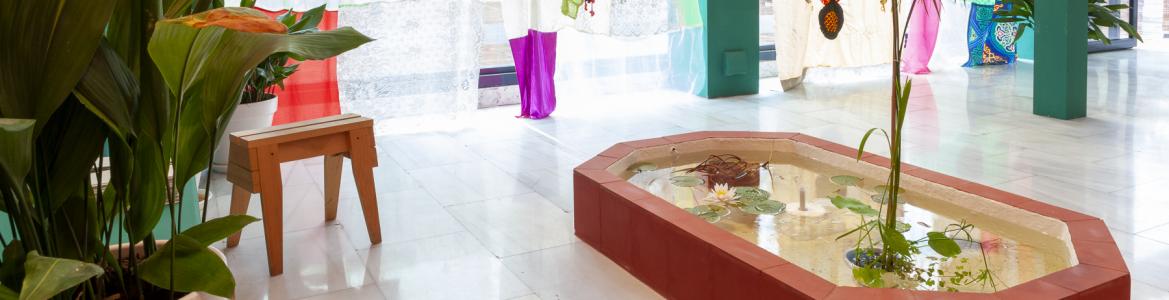 Sala  con una fuente, banco y textiles colgados de una cristalera