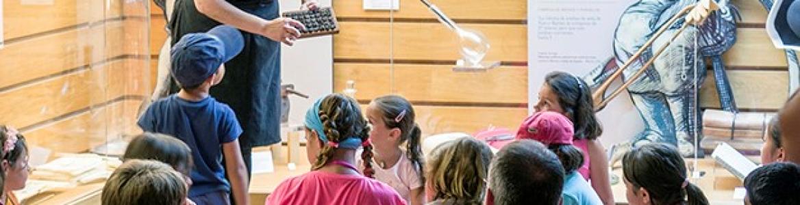 Talleres en Nuevo Baztán Niños y niñas en el centro de interpretación mirando a la educadora de la actividad que les explica cómo se hace el vídrio