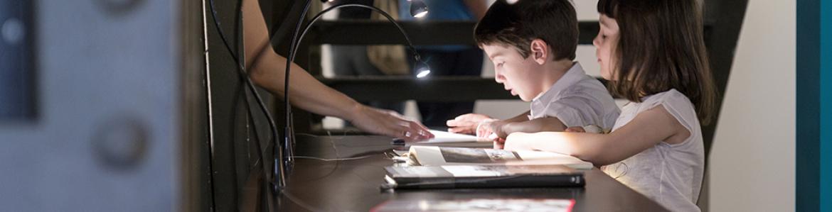 Dos niños mirando un libro en una vitrina de una sala de exposiciones