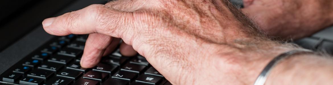 Primer plano de las manos de un hombre mayor sobre teclado de ordenador portátil