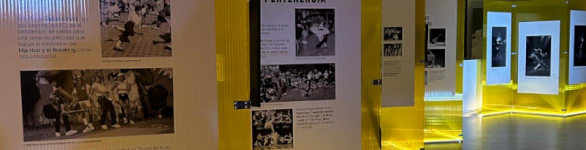 Fotografía de la sala de exposición con unos metacrilatos amarillos con fotografías en blanco y negro