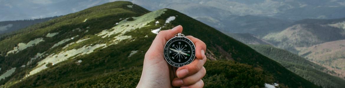buscador mano sosteniendo una brújula con paisaje de montaña al fondo