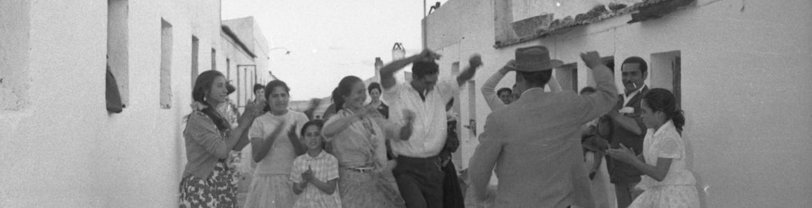 Un grupo de hombres, mujeres y niños bailando flamenco y dando palmas en un poblado