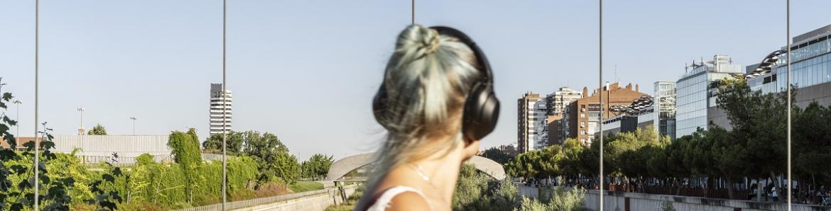 REGIÓN Eduardo Nave Mujer escuchando música con cascos, girada al espectador, en un parque rodeado de edificios