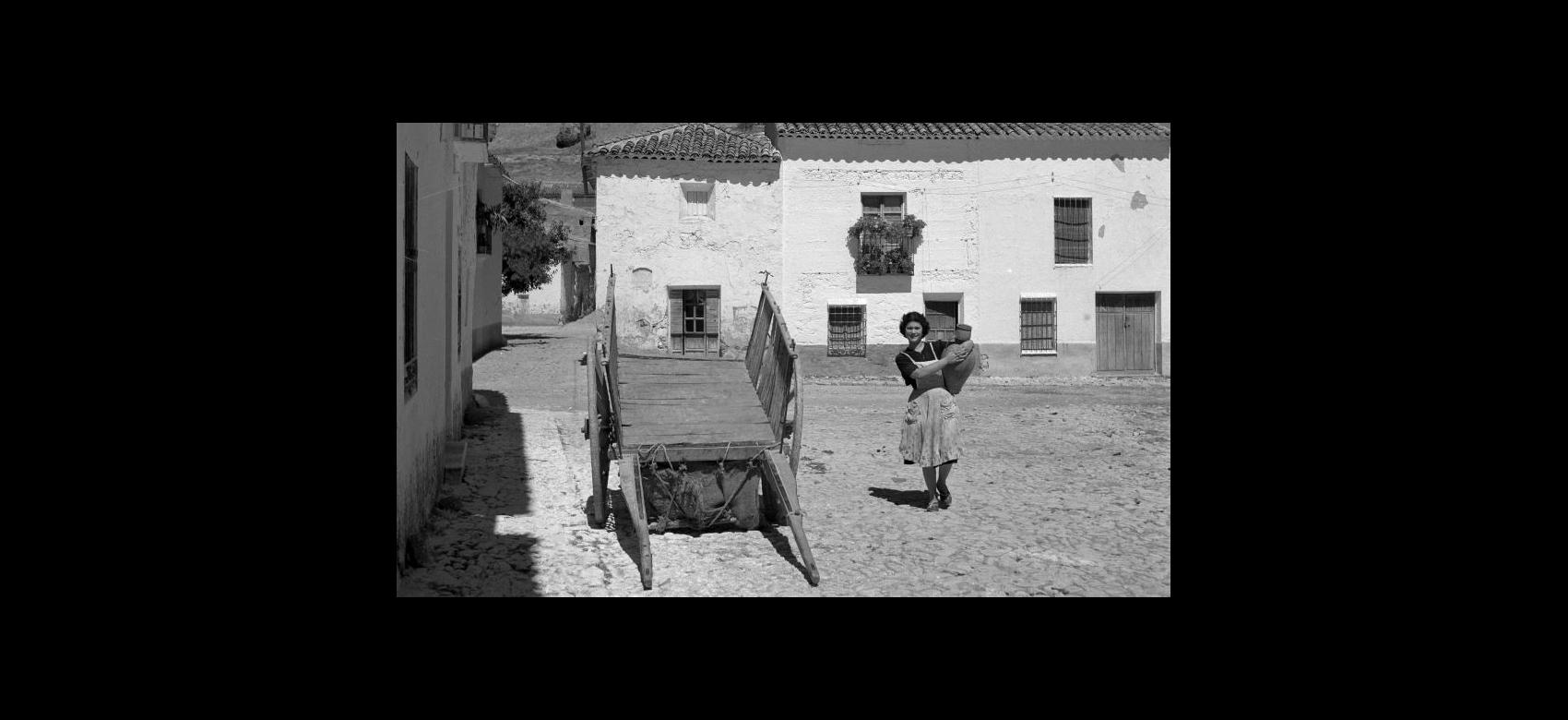 Fotografía en blanco y negro de una mujer llevando un cántaro de barro en un entorno rural