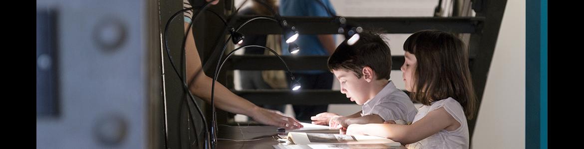 Dos niños mirando un libro en una vitrina de una sala de exposiciones