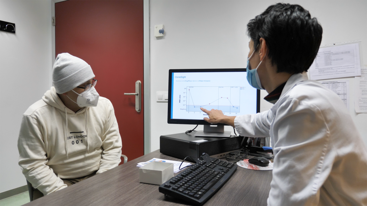 Doctora a un lado de la mesa señalando una pantalla y paciente al otro lado