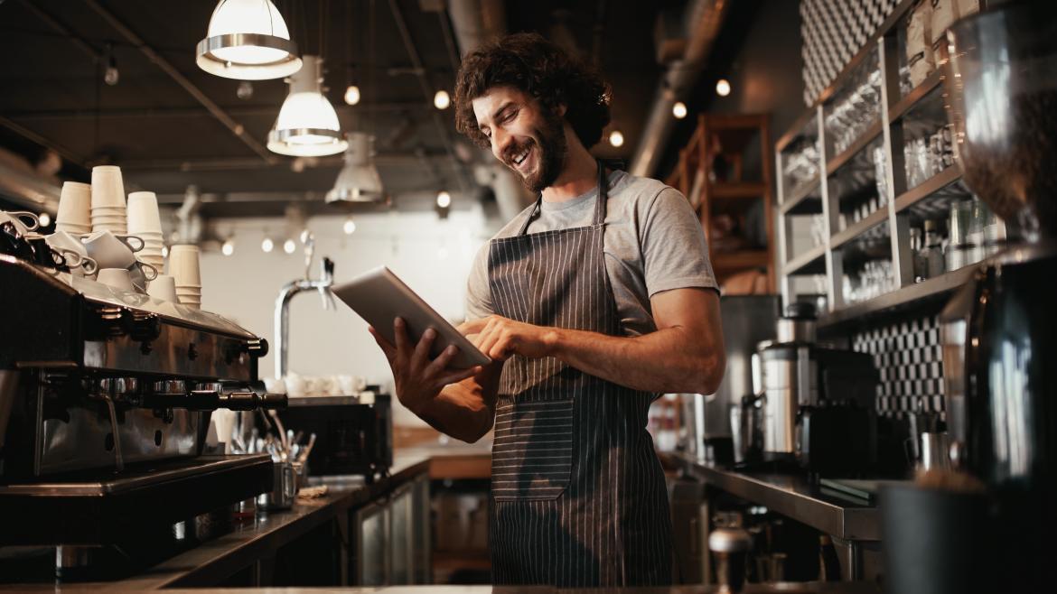 Una chico observa una tablet tras la barra de un café