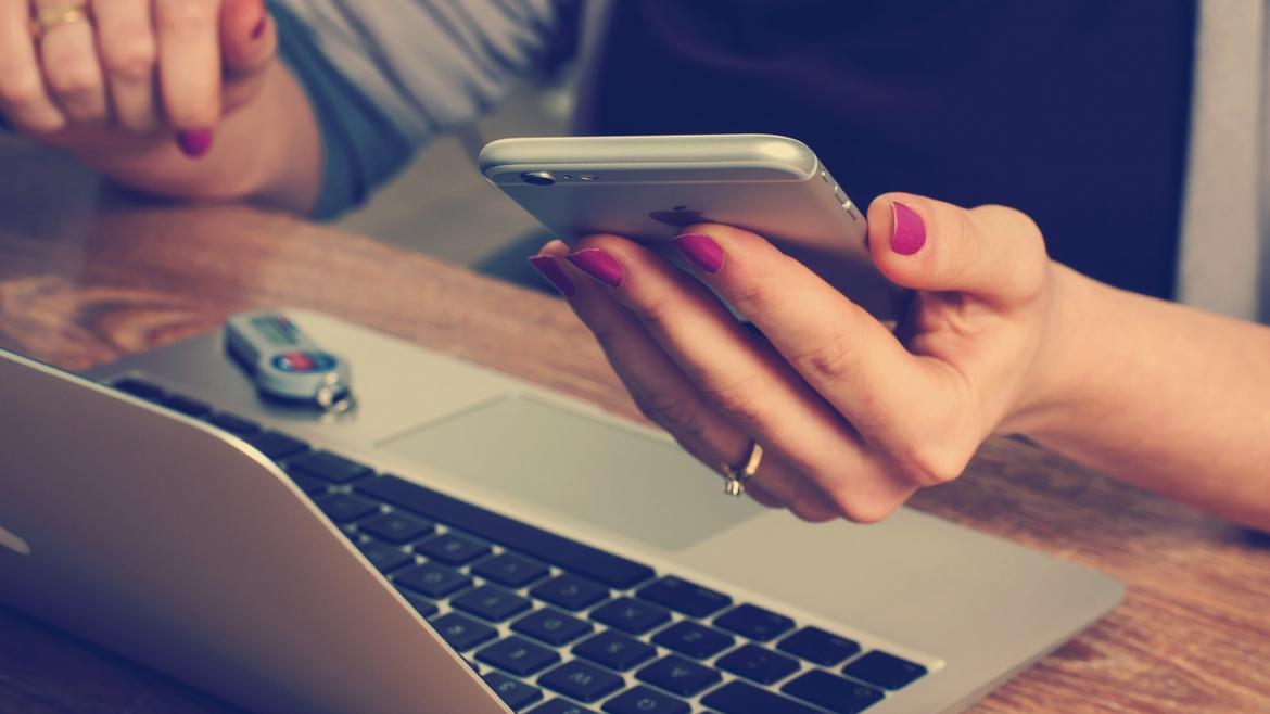 Manos de mujer con teléfono móvil y ordenador portátil