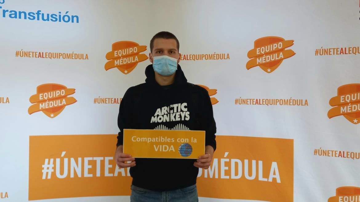 Joven posando con con cartel de donar médula y con un trasera de Equipo Médula