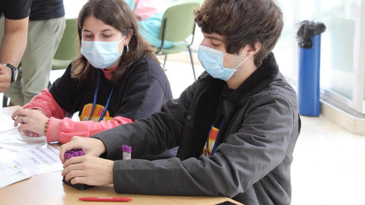 Dos alumnos sentados en la mesa informativa con tubos de sangre