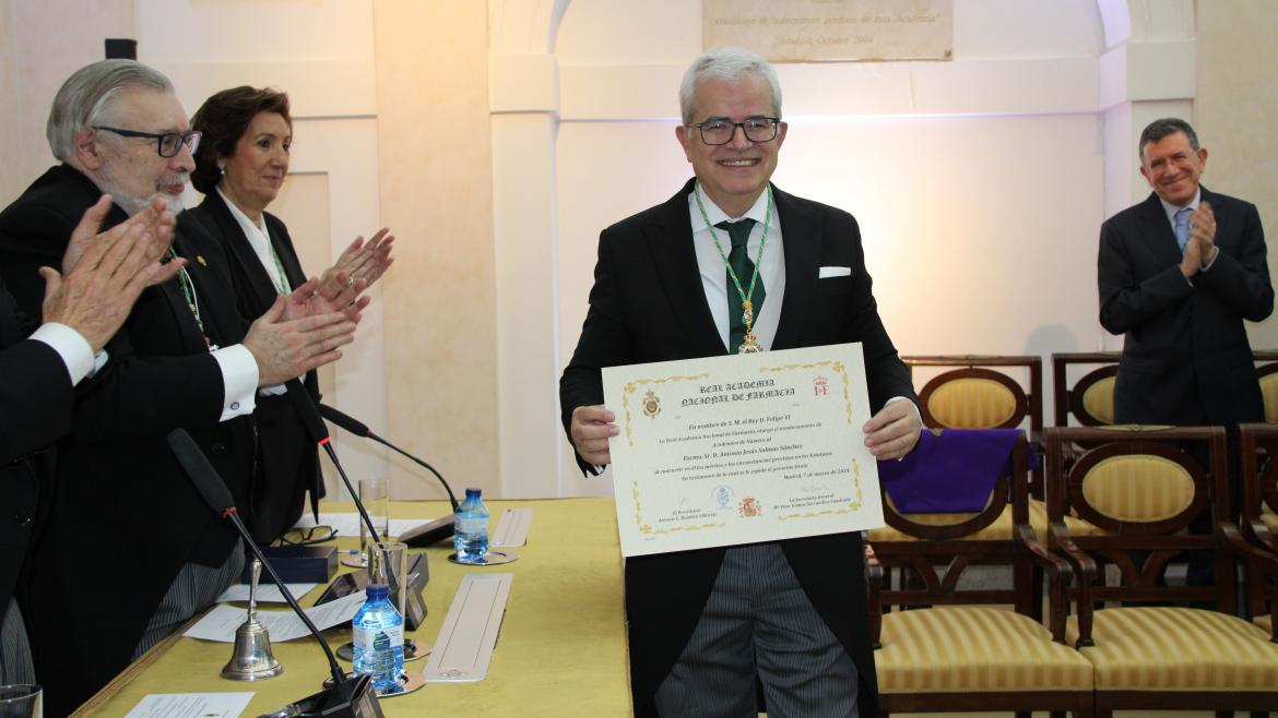 hombre vestido de gala con un diploma en la mano y personas a los lados que aplauden