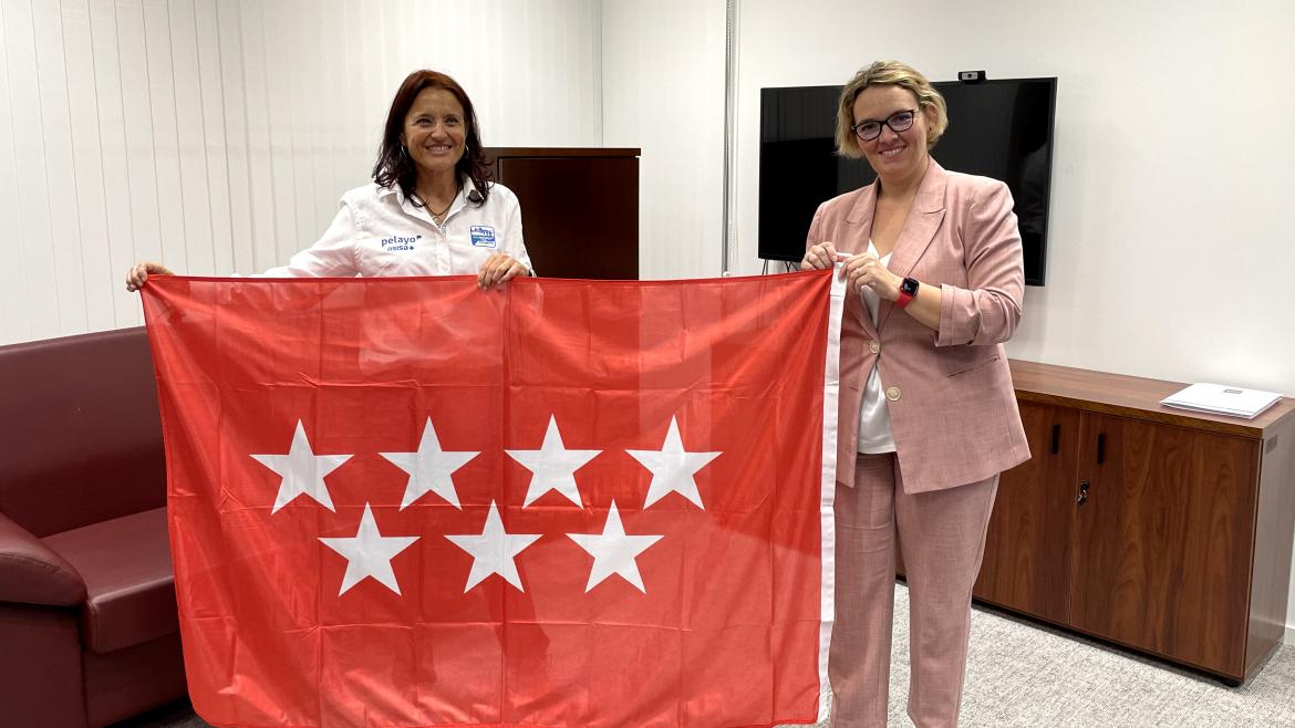 La directora y la representante madrileña posan con la bandera de la Comunidad