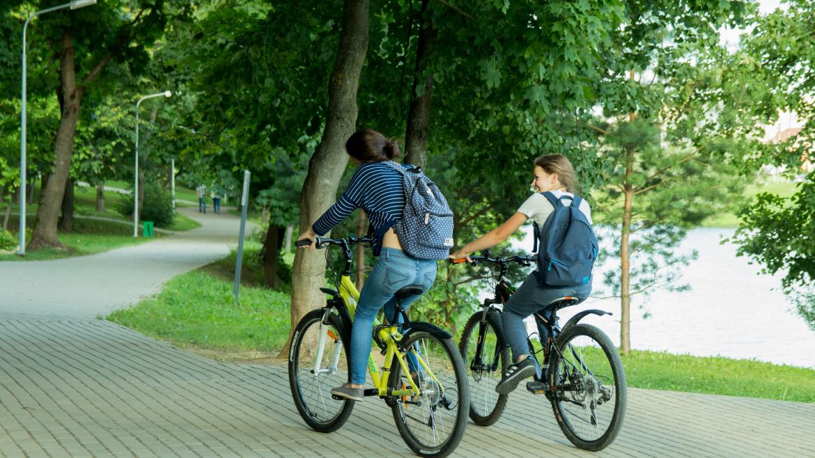 Dos chicas en bici por zona ajardinada