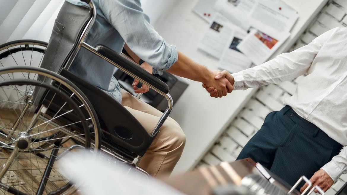 Una persona en silla de ruedas da la mano a otra que le ha contratado 