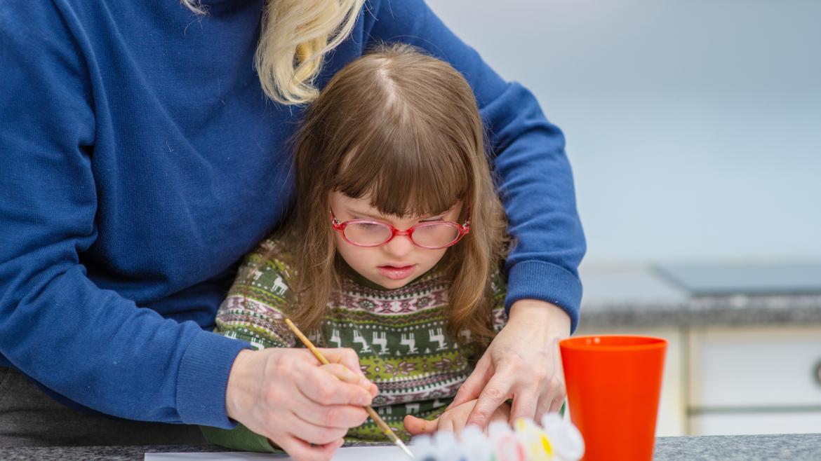 Niña con síndrome de Down pintando con ayuda de una mujer 