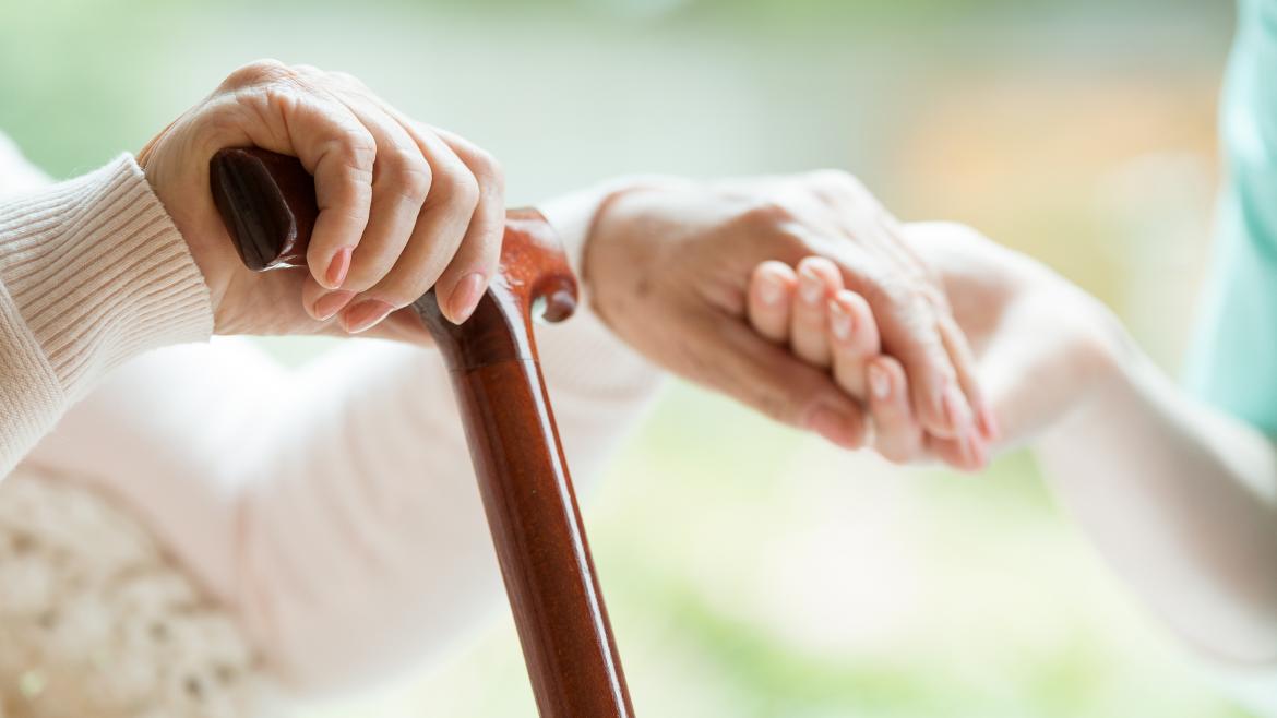 Primer plano de una mano con un bastón y la otra mano agarrando la mano de una persona más joven