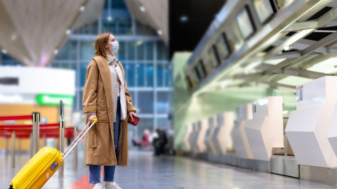 Turista mujer con maleta y mascarilla en el aeropuerto