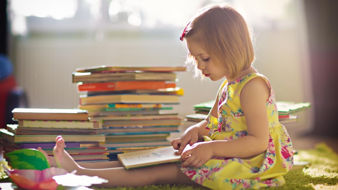 Niña sentada en el suelo con una pila de libros, leyendo Niña sentada en el suelo con una pila de libros, leyendo