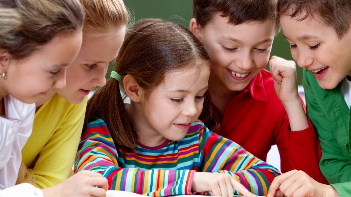 Grupo de cinco niños leyendo alrededor de un libro