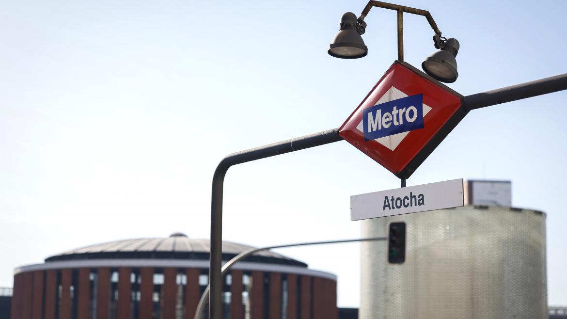 Cartel de metro con Atocha y de fondo la estación