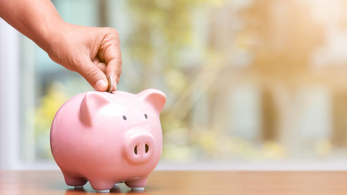 Hucha Mano metiendo dinero en una hucha con forma de cerdo
