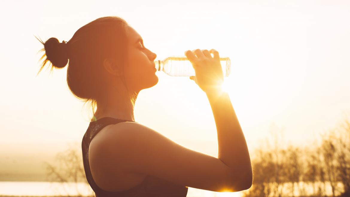 Chica bebiendo agua con sol de fondo