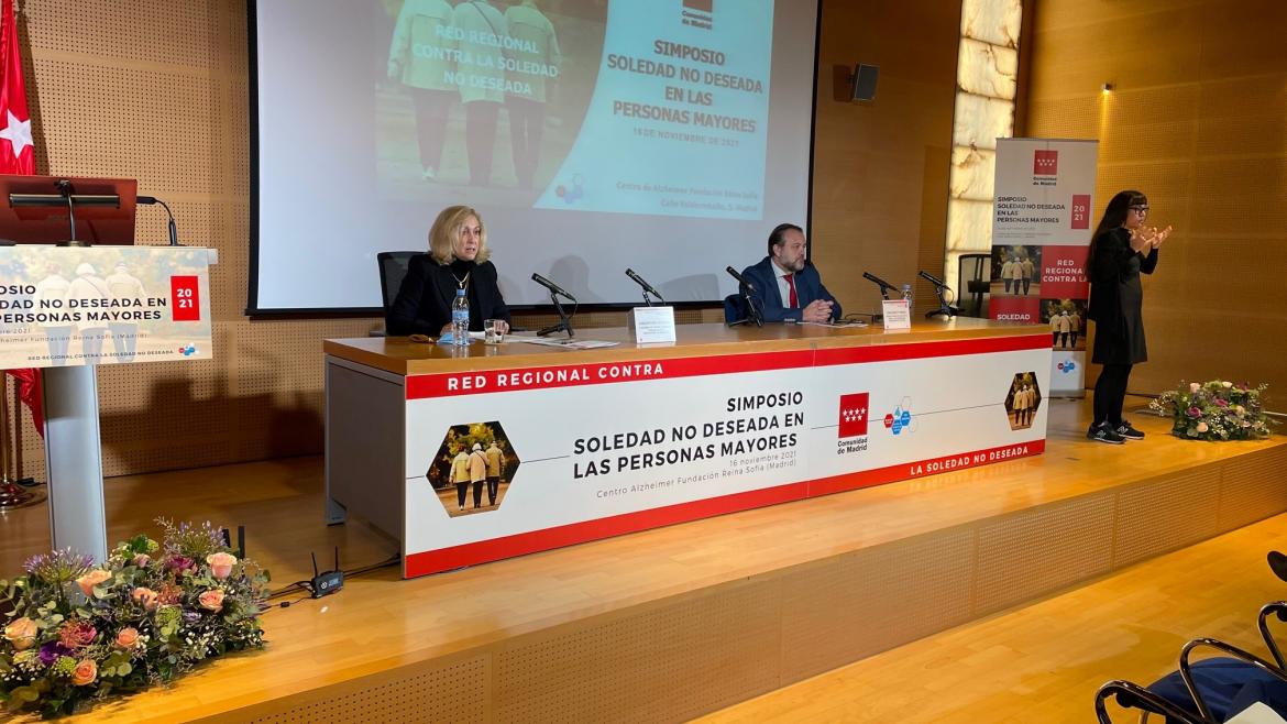 La consejera interviniendo sentada en la mesa del acto en el escenario