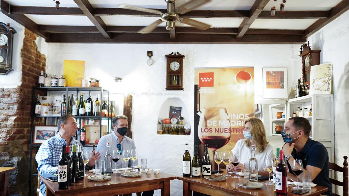 La consejera sentada en una mesa con algunas botellas y copas de vino  junto con el resto de asistentes